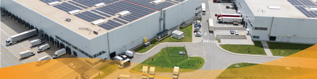 Aerial view of a modern warehouse and distribution center with rooftop solar panels, loading docks, delivery trucks, and surrounding roadways, with a translucent orange graphic overlay along the bottom of the image.